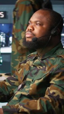 Telsiz ve uydu donanımı kullanarak savaş desteği sağlayan dikey video ordu telekomünikasyon sistemi operatörü. İletişim ağlarını yöneten askeri sevkiyat memuru, ekranlara bakıyor, kamera B