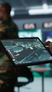 Dikey video askeri ajan kontrol odasında çalışıyor, tablet üzerinde yazılım kullanıyor, hava keşif verilerini analiz ediyor. Taşınabilir aygıtla İHA 'ları kontrol eden istihbarat uzmanlarını kapatın.