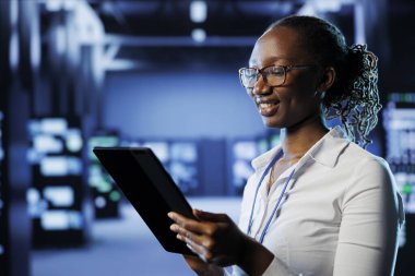 Sunucu merkezi sıraları arasında gülümseyen kadın dünya çapındaki işletmeler için işleme kaynakları sağlıyor. Devasa veritabanlarını yönetmekle görevli veri merkezinin ana bilgisayarlarının düzeltilmesi