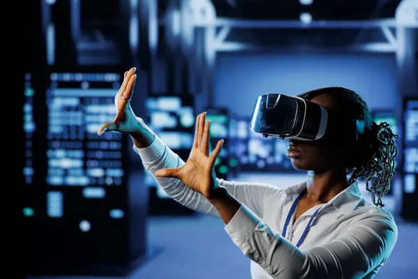 stock image Tech support in data center uses virtual reality to prevent system overload. BIPOC VR technology user in server room ensuring enough network bandwidth for smooth operations