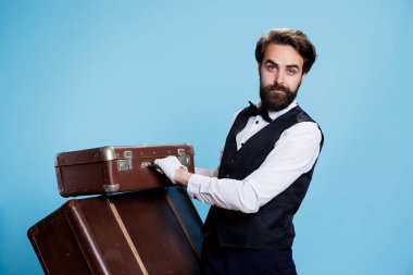 Friendly bellhop shows satisfaction, illustrating role as an approachable hotel porter for hospitality and assistance. Professional bellboy with gloves carrying bags in studio, tourism concept. clipart