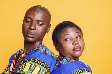 Siyahi adam ve kadın arka arkaya stüdyonun yakın plan portresini çekerken birbirlerine bakıyorlar. Turuncu arka planda ciddi yüz ifadesi olan kendinden emin Afro-Amerikan çift.