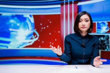 Asyalı sunucu canlı yayında haber sunuyor, haber odasındaki günlük olaylardan bahsediyor. Kadın gazeteci en son konular hakkında bilgi veriyor, medya televizyonu içeriği yaratıyor.