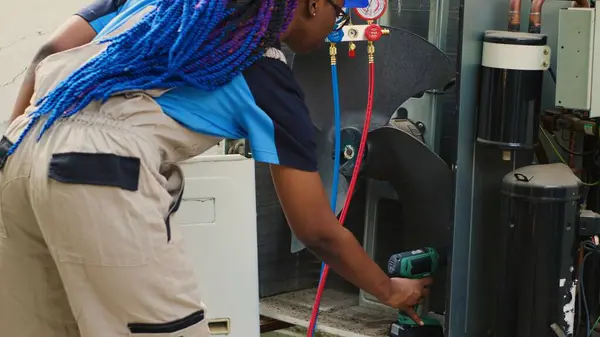 stock image Portrait of happy technician starting work on busted air conditioner, using power tool to open up condenser and connect manometers. Engineer opening hvac system to start measuring freon levels inside