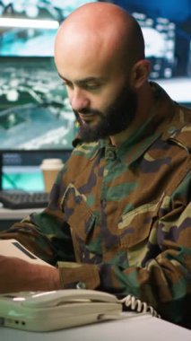 Komuta merkezindeki dikey video subayı istihbarat dosyalarına bakarken telefon alıyor. İstihbarat uzmanı rakiplerini okuyor strateji görev dosyası ve telefonla konuşuyor, kamera