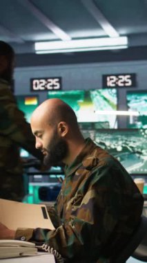 Komuta merkezindeki dikey video subayı istihbarat dosyalarına bakarken telefon alıyor. İstihbarat uzmanı rakiplerini okuyor strateji görev dosyası ve telefonla konuşuyor, kamera