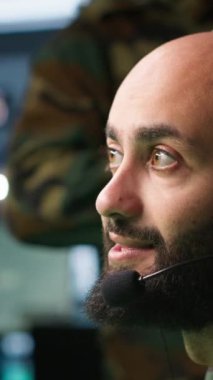 Dikey video Orta Doğu askeri harekat subayı ordu istihbarat analistlerinden cephedeki askerlere bilgi aktarıyor. Telsiz iletişim operatörü meslektaşıyla kulaklık kullanarak tartışıyor.