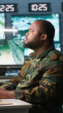 Dikey video askeri ajan kontrol odasında çalışıyor, hava keşif verilerini analiz ediyor ve meslektaşımla konuşuyor. İstihbarat elemanı ekranları kontrol ediyor, iş arkadaşı, kamera A ile tartışıyor.