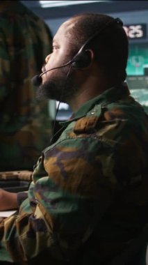 Askeri harekat subayı askeri istihbarat analistlerinden cephedeki askerlere bilgi aktarıyor, yakın çekim. Üniformalı telsiz iletişim operatörü mikrofon ve kamera B ile konuşuyor.