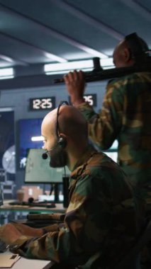 Telsiz ve uydu ekipmanı kullanan dikey video ordu telekomünikasyon operatörü. İletişim ağlarını yöneten Ortadoğu askeri sevkiyatçısı, ekranlara bakıyor, kamera B