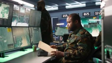 Görev kontrol merkezindeki askeri asker ulusal güvenlik operasyonlarını denetliyor, klasör dosyalarını okuyor. Afro-Amerikan ordu uzmanı izleme odasındaki verileri kontrol ediyor. Kamera B