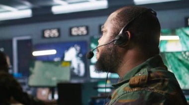 Askeri sevkiyat memuru, ön saflarda savaşan komutanlara bilgi vermek için kulaklık mikrofonu kullanıyor. Operasyon üssündeki birliklere istihbarat sağlayan ordu uzmanı, kamera B