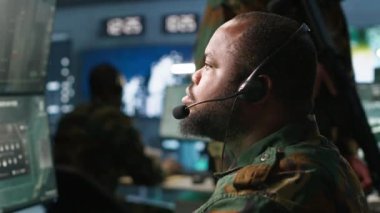 Telsiz ve uydu teçhizatı kullanarak savaş desteği sağlayan ordu telekomünikasyon sistemleri operatörü. Askeri sevk memuru iletişim ağlarını yönetiyor, ekranlara bakıyor, kamera A