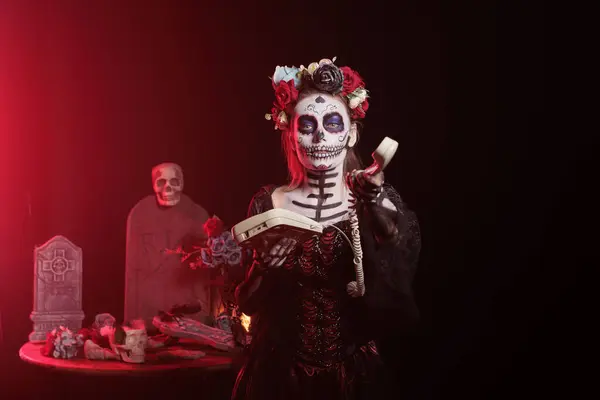 stock image Woman talking on office cord telephone at Day of the Dead event to remember the deceased. Lady using landline phone to answer call during Mexican holiday of remembrance for those who have passed