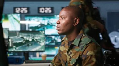 Askeri üste dijital radar ekipmanları ve çalışan füze sistemleri ile gözetleme yapan bir istihbarat ajanı. Afrika kökenli Amerikalı bir adam, ordu merkezinin güvenlik kameralarını, izinsiz hareketler için izliyor. Kamera A.