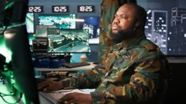 Telsiz ve uydu teçhizatı kullanarak savaş desteği sağlayan ordu telekomünikasyon sistemleri operatörü. İletişim ağlarını yöneten askeri sevkiyat memuru, ekranlara bakıyor, kamera B