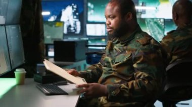 Görev kontrol merkezindeki askeri asker ulusal güvenlik operasyonlarını denetliyor, klasör dosyalarını okuyor. Afro-Amerikan ordu uzmanı izleme odasındaki verileri kontrol ediyor. Kamera A.