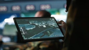 Askeri ajan kontrol odasında çalışıyor, tablet üzerinde yazılım kullanıyor, hava keşif verilerini analiz ediyor. Taşınabilir cihazlı İHA 'ları kontrol eden istihbarat uzmanlarını kapatın. Kamera A