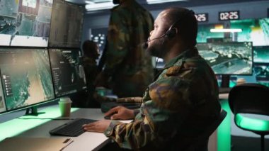 Askeri sevkiyat subayı, ordu istihbarat analistlerinden cephedeki birliklere bilgi aktarıyor, yakın çekim. Üniformalı telsiz iletişim operatörü mikrofon ve kamera B ile konuşuyor.