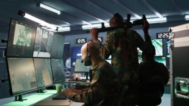 Telsiz ve uydu teçhizatı kullanan ordu telekomünikasyon sistemi operatörü. İletişim ağlarını yöneten Ortadoğu askeri sevkiyatçısı, ekranlara bakıyor, kamera B