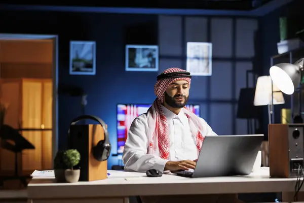 stock image Arab businessman typing on his laptop at a trendy workstation. In a peaceful and professional workplace atmosphere, a Muslim man is browsing, communicating via email, and using WiFi connectivity.