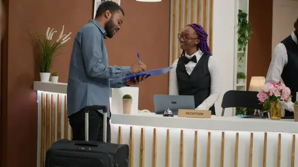 stock image Guest filling in registration forms and signing papers before seeing room, finishing with check in. Employee providing luxurious concierge services, greeting people at front desk. Handheld shot.