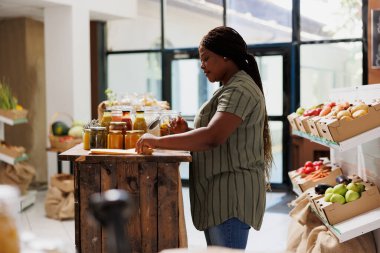Afrikalı Amerikalı bir müşteri süpermarkette durmuş kağıt torbasını doldurmak için çevre dostu ve yerel ürünler arıyor. Siyahi kadın cam kaplarda çeşitli organik ürünler seçiyor..