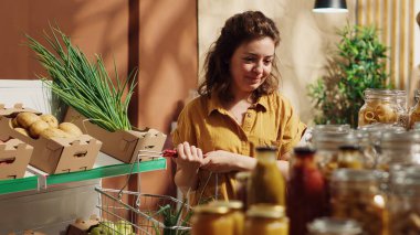 Vegan woman in specialty zero waste supermarket tasting pantry items before adding them to shopping basket. Client in local shop trying out food to determine if its toxins free before buying clipart