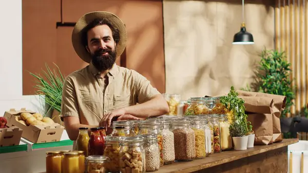 stock image Portrait of smiling vegan man in eco friendly zero waste supermarket using shopping basket to purchase bulk items in ecological containers. Client in local bio grocery shop buying additives free food