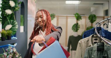 Tracking shot of customer dancing in clothing store during promotional season after finding cheap garments. Woman excited about sales in fashion boutique, leaving with shopping bags full of clothes clipart