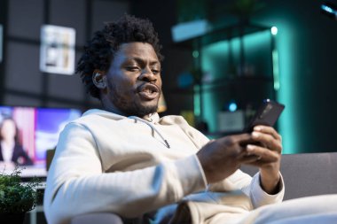 İnternetten arkadaşlarıyla telefonda sohbet eden mutlu bir insan şık bir evde hoş geldin diyor. Afrika kökenli Amerikalı bir adam sosyal medya hesabına kayıyor, eğleniyor.