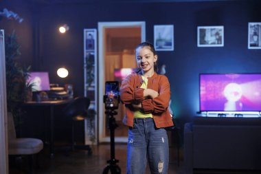 Sosyal medya için tripodla akıllı telefonla video çekerken dans eden ve şarkı söyleyen Z kuşağı kızları eğlendiriyor. Gülümseyen çocuk telefonla kaydedilen profesyonel koreografiyle takipçilerini eğlendiriyor