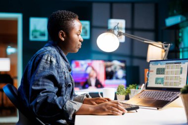 Afro-Amerikalı yatırımcı portatif bilgisayarda oturmuş ticaret grafiklerine ve borsaya bakıyor. Ekonomik grafiği inceleyen siyahi kadın dizüstü bilgisayarındaki yatırım artışını gösteriyor.