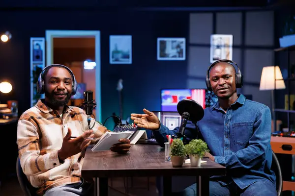 stock image African american male vloggers, discussing various topics and interacting with fans, using professional recording equipment to produce high quality content for online streaming services.