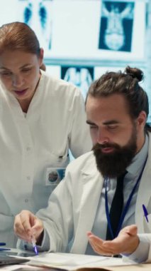 Hastalıklara karşı tedavi planı bulmak için meslektaşı ile birlikte çalışan dikey videodaki doktor, tıp kabinesindeki hemşirelerden hoşnutsuzmuş gibi davranıyor. Analiz ve test sonuçları inceleniyor