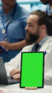 Kroma anahtar ekranının yanında hastane kayıtlarına bakan doktorların dikey video grubu teşhisi incelemek için x ışını test sonuçlarını kullanıyor. Tedavi için özel klinikte çeşitli uzmanlar toplandı