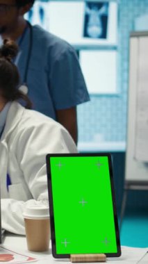 Doktorlardan oluşan dikey video ekibi, tıbbi dolaptaki bilgisayarın yanında analitiğe danışarak teşhisi bulmak için röntgen sonuçlarını inceliyor. Lisanslı sağlık görevlileri masasındaki hastane kayıtlarını inceliyor.