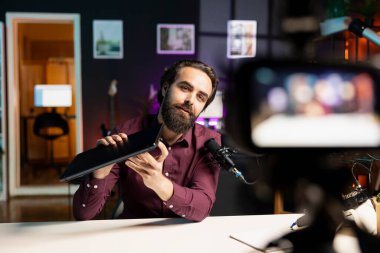 Seyircilere dizüstü bilgisayar sunan adam profesyonel kamera ve mikrofonla video çekiyor. İçerik oluşturucu dizüstü bilgisayar ürünlerini değerlendiriyor, stüdyo ortamında özel ekipmanlarla kayıt yapıyor