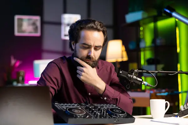 stock image Artist filming DJ mixing tutorial, thinking of examples of sampling on sound controller to teach audience. Man contemplating if mixer musical equipment deserves endorsement