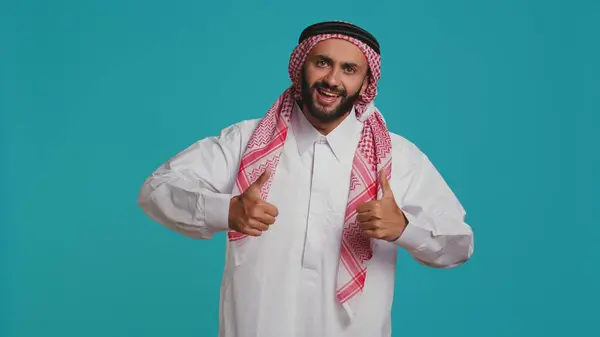 stock image Person wearing customary thobe and kufiyah seems joyful, exhibiting genuine muslim beliefs and practices. Middle eastern guy with distinctive culture, dress and structured scarf.