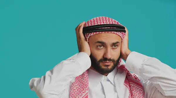 stock image Person does three wise monkeys sign in studio, wearing islamic traditional attire and headscarf. Young adult covering his eyes, mouth and ears to create metaphor sign, concept.