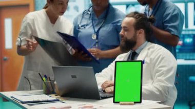 Krom anahtar ekranının yanındaki hastane kayıtlarına bakan bir grup doktor teşhisi incelemek için x ışını test sonuçlarını kullanıyor. Çeşitli uzmanlar tedavi planı için özel klinikte toplanıyorlar. Kamera A.