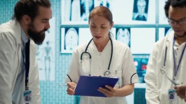 Kabinede test sonuçları ve sağlık kayıtlarını karşılaştıran uzman doktorlar, hastalık önleme konusunda meslektaşlarına danışıyorlar. Muhtelif sağlık görevlileri bir toplantıda profesyonel uzmanlıklarını paylaşıyorlar. Kamera A.