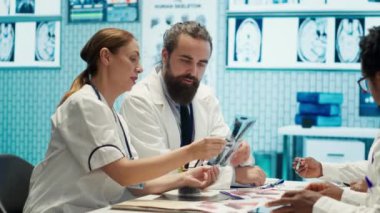Tedavi protokolleri ve iyileştirmeleri tartışan bir toplantıda sağlık uzmanları. Doktorlar ve hemşireler tıbbi hizmetlerin kalitesini arttırmak için özel bir klinikte teşhis sonuçlarını değerlendiriyorlar. Kamera A.