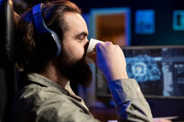 IT specialist drinking coffee with headphones on listening to songs, scripting artificial intelligence on computer. Developer enjoying hot beverage and music in ears while working on coding AI on PC clipart