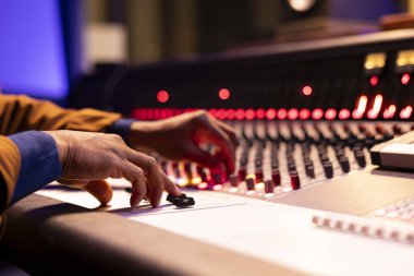 Profesyonel stüdyoda ses karıştırıcı ve konsol kullanan müzik mühendisi, düğmelere basarken ses seviyelerini ayarlıyor ve kontrol panelindeki düğmeleri çeviriyor. Teknisyen düğmelerle çalışır. Kapat..