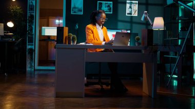 Afrikalı Amerikalı öğrenci evde okul ödevleri üzerinde çalışıyor, son bekarlığa veda ödevi için önemli bilgileri araştırıyor. Masada proje ödevi yazan genç bir kadın. Kamera B.