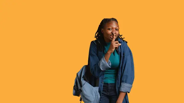 stock image Stern african american woman doing shushing hand gesturing, irritated by noise, having negative mood. Girl placing finger on lips, doing quiet sign gesture, studio background, camera B