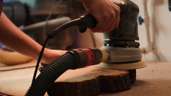 stock image Craftsperson works with orbital sander on lumber block to achieve smooth finish, close up shot. Woodworking specialist in furniture assembly shop using angle grinder to fix wooden surface, camera A