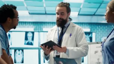 Doktorlar sağlık kayıtlarını ve röntgen taramalarını görüşmek için tedavi merkezinde buluşuyorlar. Lisanslı sağlık görevlileri hastalık önleme, takım çalışması ve uzmanlık testleri üzerinde yoğunlaşıyor. Kamera A.